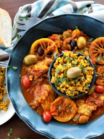 Moroccan chicken with rice in blue bowl, rice on white plate with fork and knife, bread and napkin